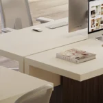 Caesarstone ICON 4001 Fresh Concrete in Minimalist white desks with computers, office chairs, magazines, and green plant leaves in bright workspace.