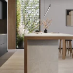 Caesarstone Quartz 4011 Cloudburst Concrete surface in Minimalist kitchen with black cabinets, wooden island, stool, decorative plants, abstract wall art, and scenic window view.