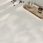 Caesarstone Quartz 4600 Organic White surface in Clear glass and espresso on a wooden tray with scattered coffee beans on white surface.