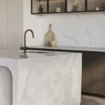 Caesarstone Quartz 5031 Statuario Maximus surface in Minimalist kitchen with marble island, modern faucet, wooden stools, and open shelving with dishes.