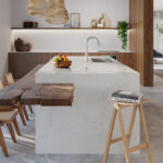 Caesarstone ICON 5131 Calacatta Nuvo surface in Modern kitchen with wooden cabinets, marble island, bar stools, built-in ovens, and a large plant.