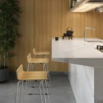 Caesarstone ICON 5131 Calacatta Nuvo surface in Minimalist kitchen with marble island, wooden bar stools, built-in stove, and large potted plant.