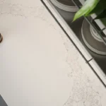 Teapot, cup of tea, leaf plant, plates, and chair on Caesarstone ICON 5131 Calacatta Nuvo white marble tabletop.