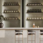 Caesarstone Quartz 6131 Bianco Drift surface in Minimalist bar with four stools, illuminated shelves displaying bottles, and a potted plant.