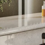 Caesarstone Quartz 6131 Bianco Drift surface in Marble countertop with a decanter, two glasses, a chair, and a leafy plant nearby.
