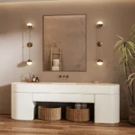 Minimalist bathroom vanity with oval sink, wall mirror, pendant lights, wicker baskets, and a potted plant.